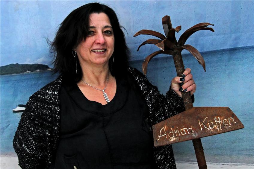 Birgit Küffen mit der Palme für das Grab ihres Mannes. Auch die Fototapete im Hintergrund erinnert an die gemeinsamen Urlaubsreisen des Ehepaars. Bild: Zibulla